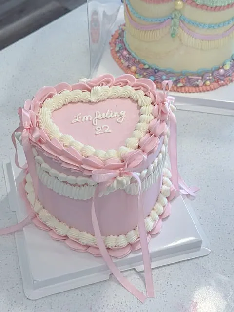 Pink heart cake with piped cream, satin bows and birthday lettering