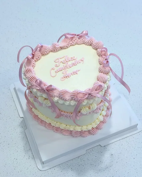 Pink heart-shaped cake with a white center, piped border, and ribbon-like pink loops.