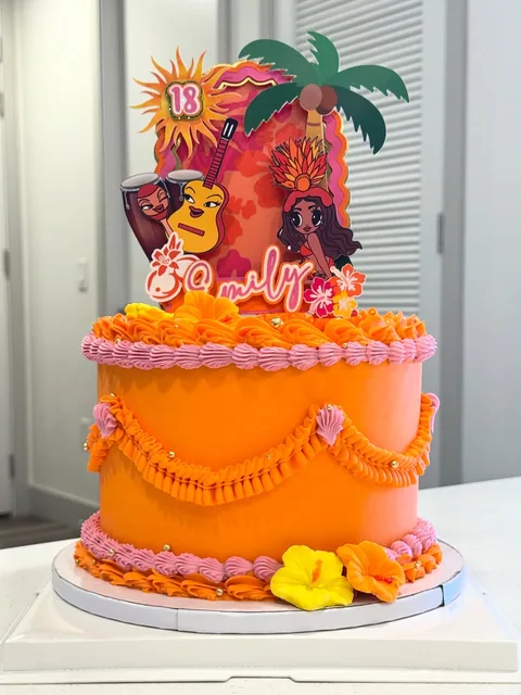 Orange two-tier cake with a colorful illustrated topper, piped borders, and a small yellow flower at the base.