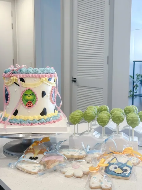 Decorated pastel cake shown beside green cake pops and assorted decorated cookies.
