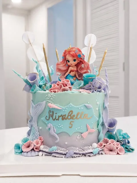 Lavender and blue cake with a mermaid topper, shell-like details, and piped pink accents.