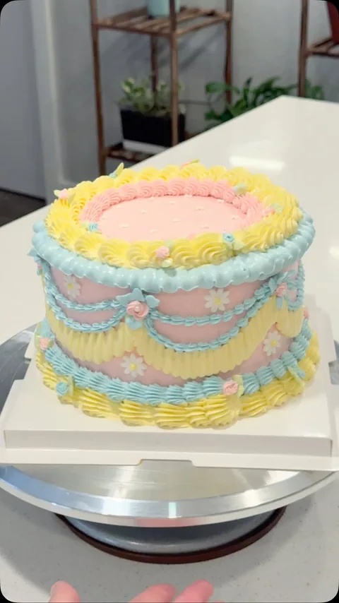 Pastel single-tier cake with scalloped piped bands in blue, yellow, and pink.