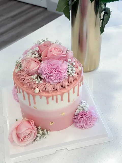 Pink and white drip cake with pink roses, carnations and small white flowers
