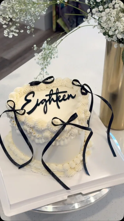 White cake with a black ribbon bow, black script lettering, and small black accents.