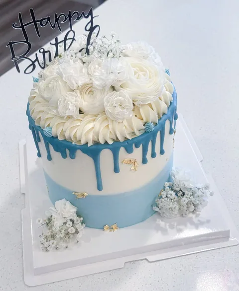 White cake with a blue drip edge, white flowers, and a black script topper.