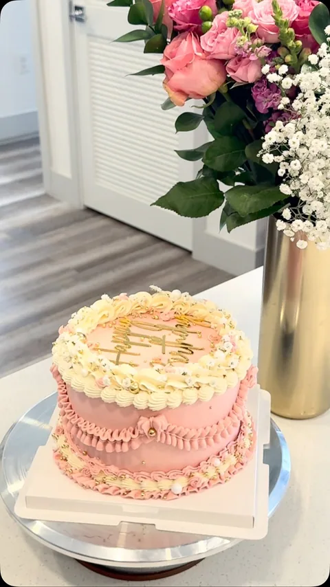 Pink vintage cake with pale yellow piped borders and gold accents, with a separate bouquet behind the cake.