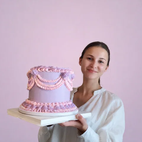 Nicka holding her purple cake, photographed against a pink background