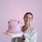 Nicka holding her purple cake, photographed against a pink background
